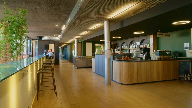 Vue d'ensemble du bar intérieur avec tabourets hauts, plantes et pancarte service au bar